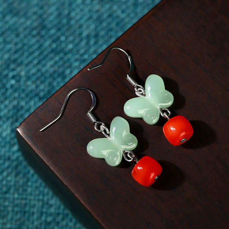 Butterfly drop earrings resting on dark wood beside blue fabric
