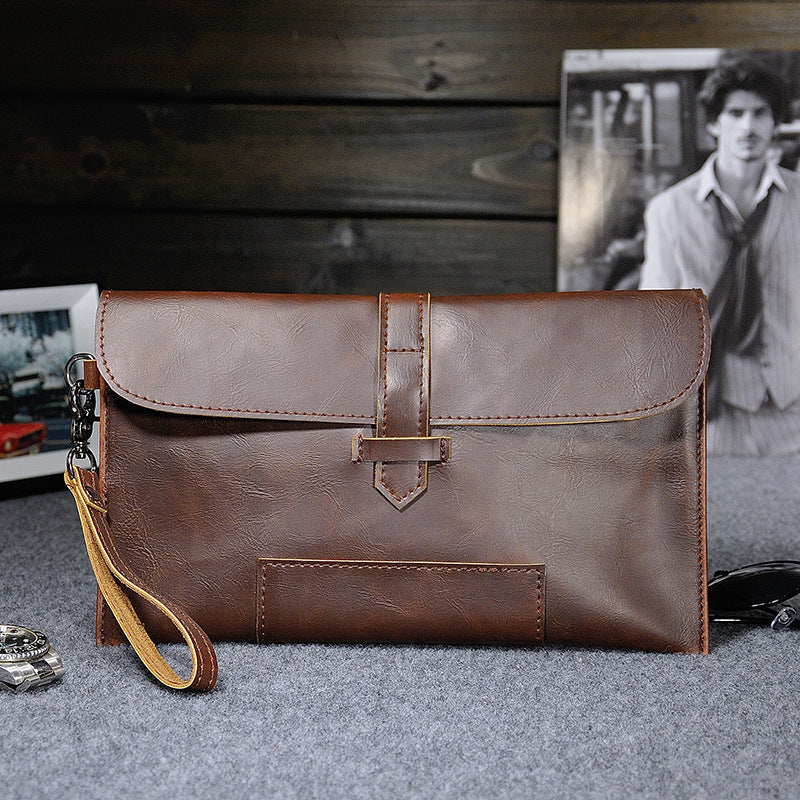 Brown faux-leather clutch with wrist strap on a gray surface