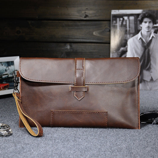 Brown faux-leather clutch with wrist strap on a gray surface