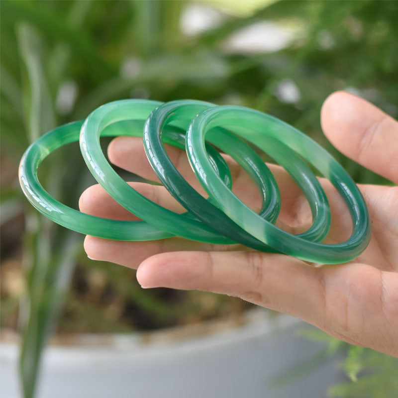Several green bangles displayed in a hand outdoors