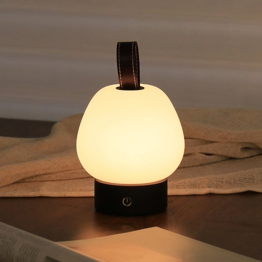 Illuminated pear-shaped lamp with dark base and loop handle on a bedside table