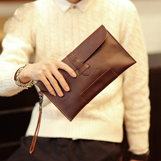 Person holding a brown envelope clutch with a wrist strap