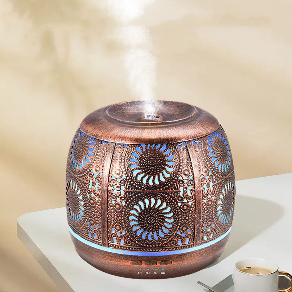 Bronze-tone floral aroma diffuser emitting mist on a light table