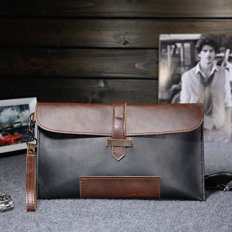 Black and brown two-tone clutch with wrist strap on a gray surface