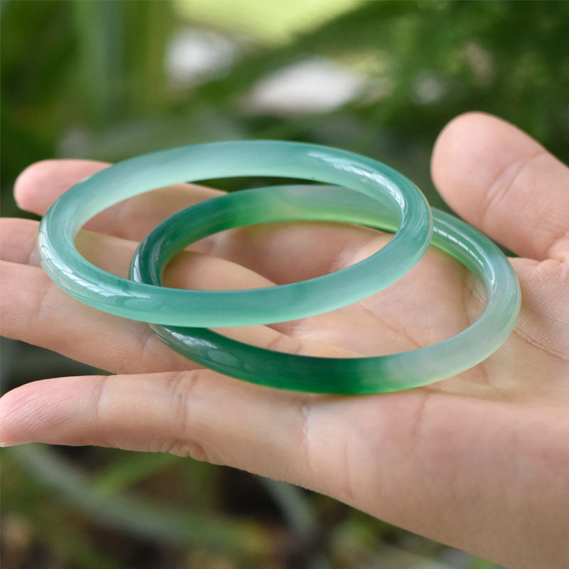 Two pale green translucent bangles held in a hand
