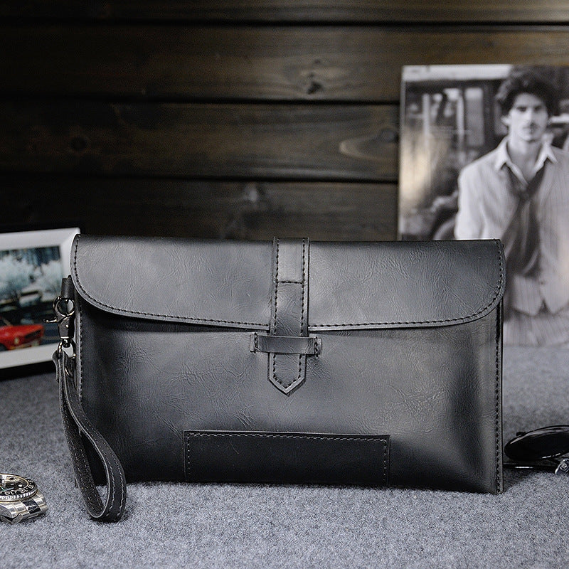 Black faux-leather clutch with wrist strap on a gray surface