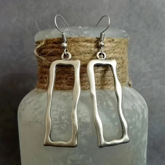 Antique silver-tone open rectangle earrings hanging on a glass jar
