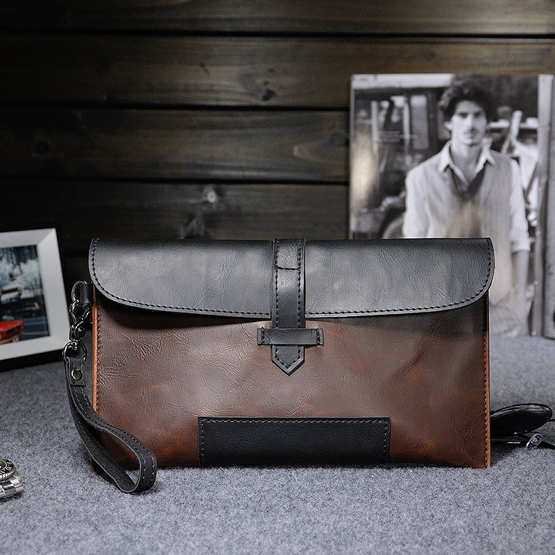 Two-tone brown and black clutch with wrist strap on a gray surface