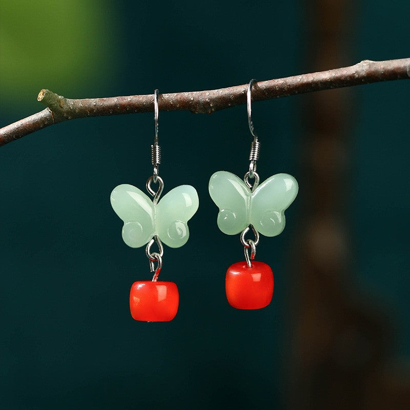 Mint-green butterfly earrings with red drops hanging from a branch
