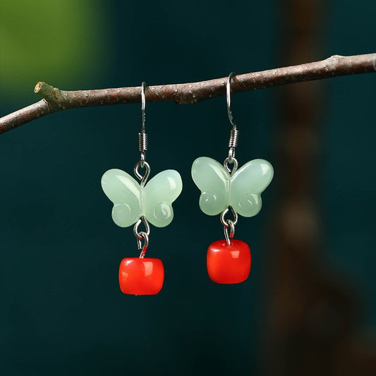 Mint-green butterfly earrings with red drops hanging from a branch