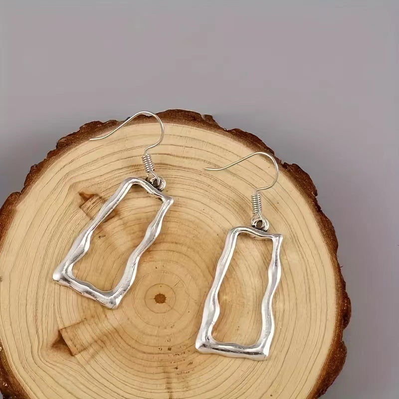 Open rectangle drop earrings displayed on a wooden slice