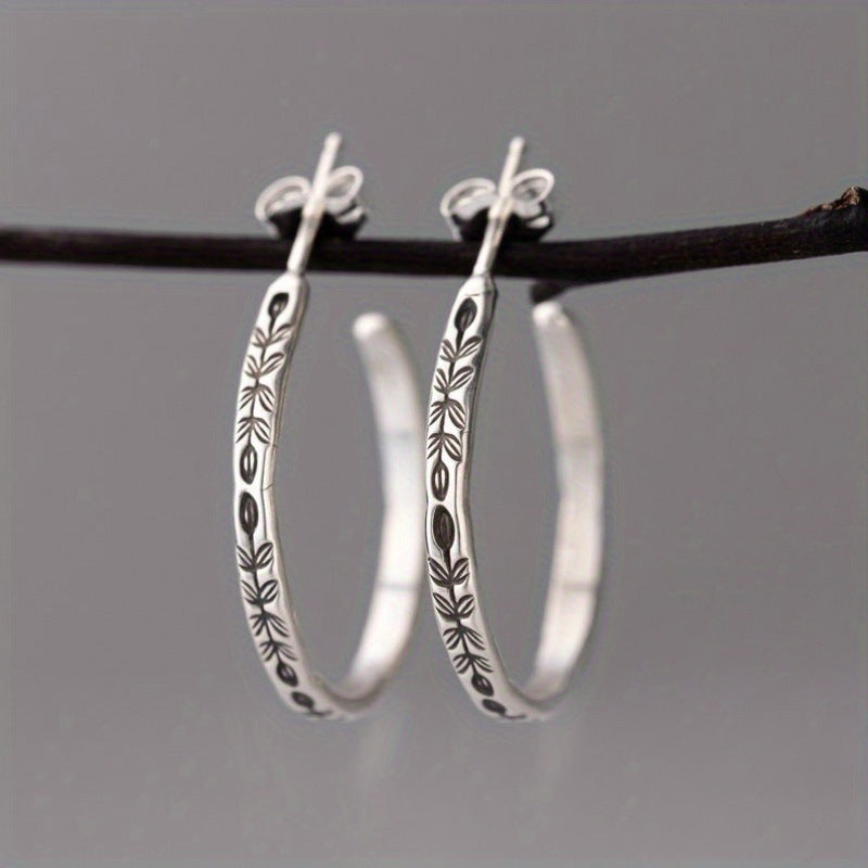 Silver-tone botanical hoop earrings hanging from a branch against gray