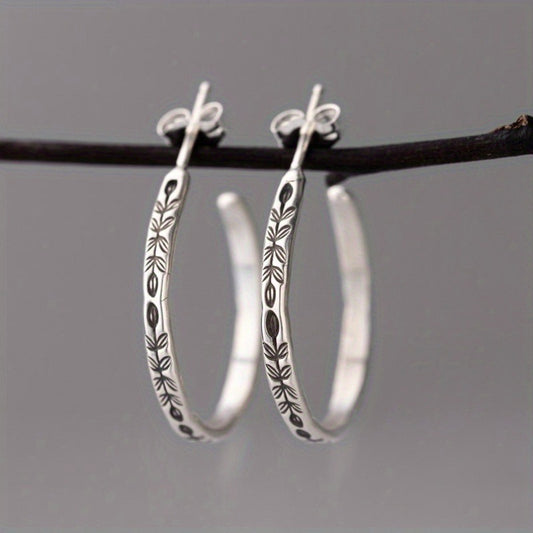 Silver-tone botanical hoop earrings hanging from a branch against gray